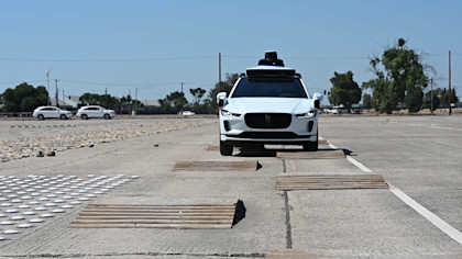 A photo of a white, Waymo vehicle undergoing durability testing at a closed course facility