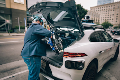 Bill Nesper, executive director of the League of American Bicyclists, loading a collapsed Brompton bike into the trunk of a Waymo vehicle