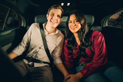Max and Lilian holding hands and smiling in the backseat of a Waymo One autonomous ride-hailing vehicle