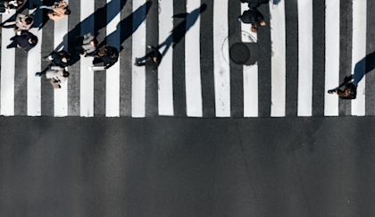 Aerial view of people at a cross walk and a Waymo vehicle waiting for them to cross.