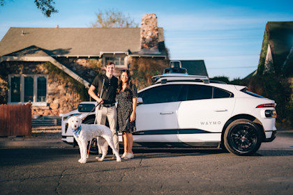 Max and Lilian posing with their dog in front of a Waymo One autonomous ride-hailing vehicle